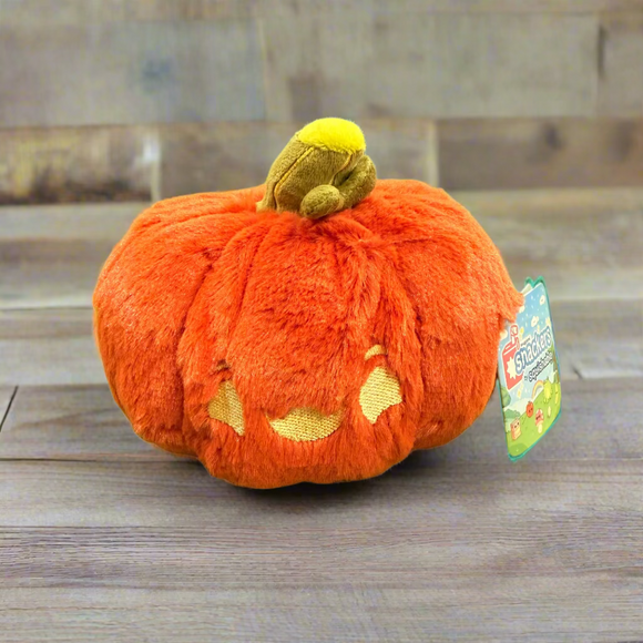 Plush pumpkin toy with a tag on a green surface, likely in a store or market setting.